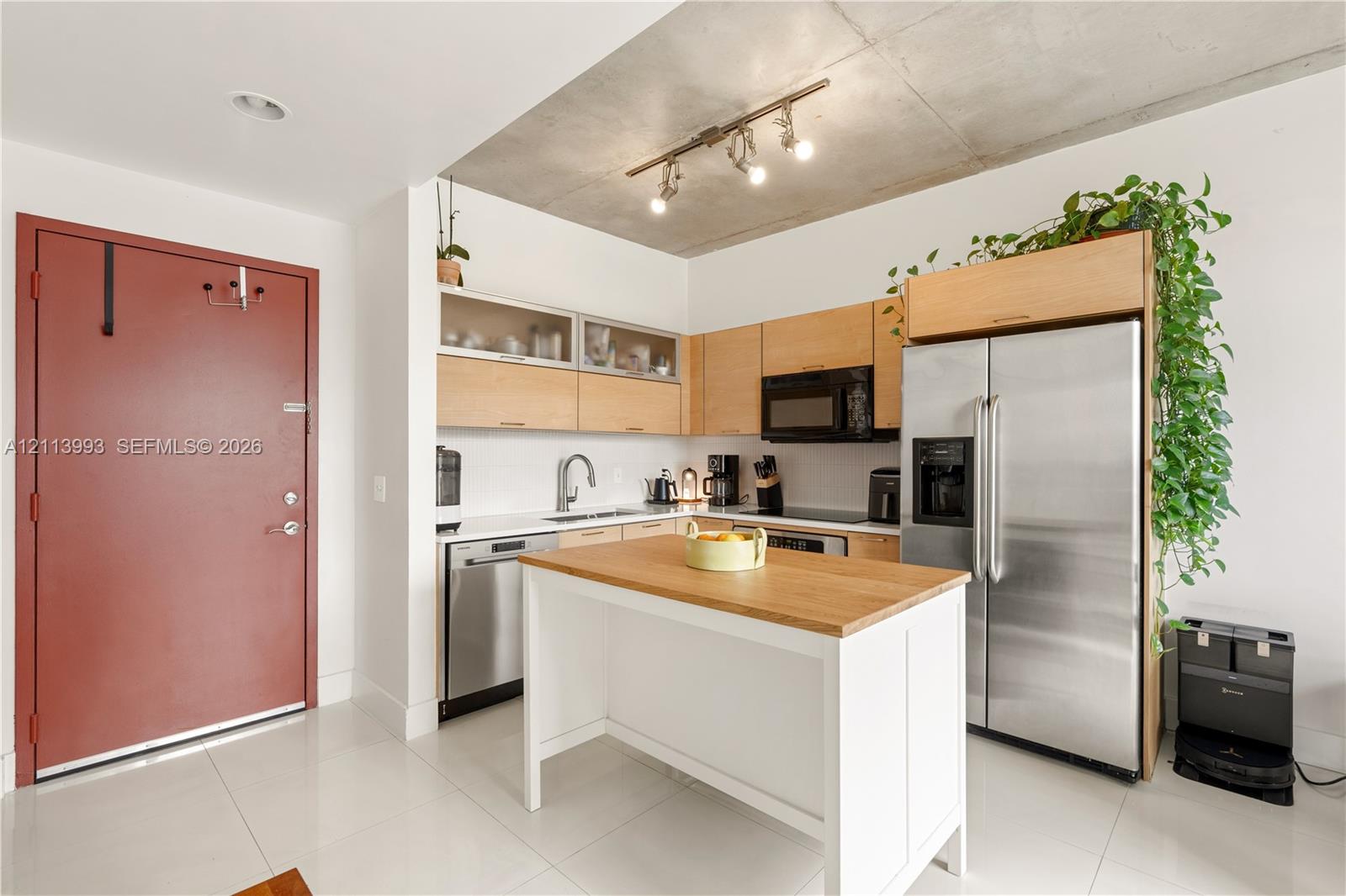 Kitchen featuring light wood-finish cabinetry, white solid-surface countertops, industrial-style exposed concrete ceiling, stainless steel appliances, and a central prep island