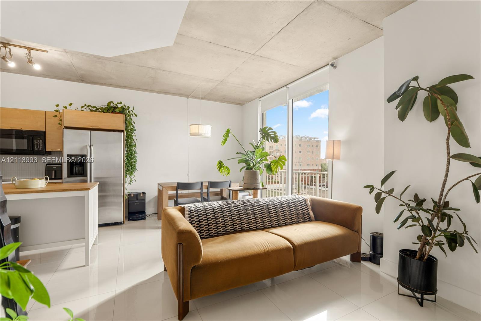 Exposed concrete ceiling, floor-to-ceiling glass sliding door, polished tile flooring, stainless steel kitchen appliances, and light-toned cabinetry