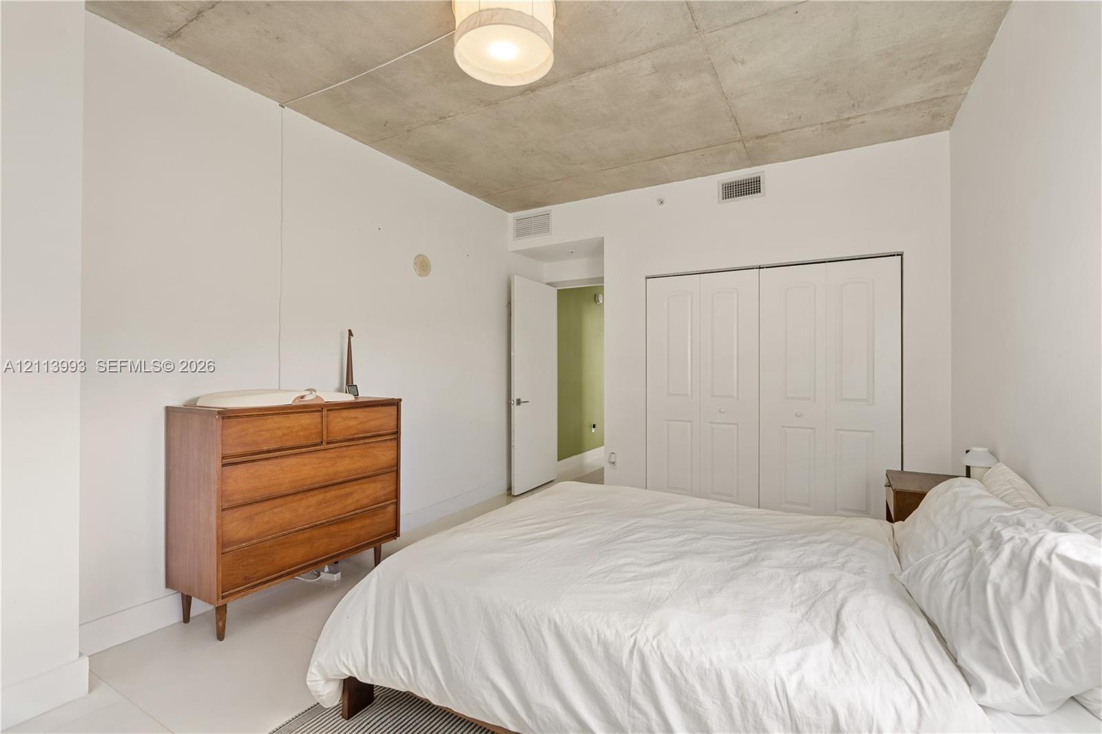 Exposed concrete ceiling, white walls, and built-in double-door closet