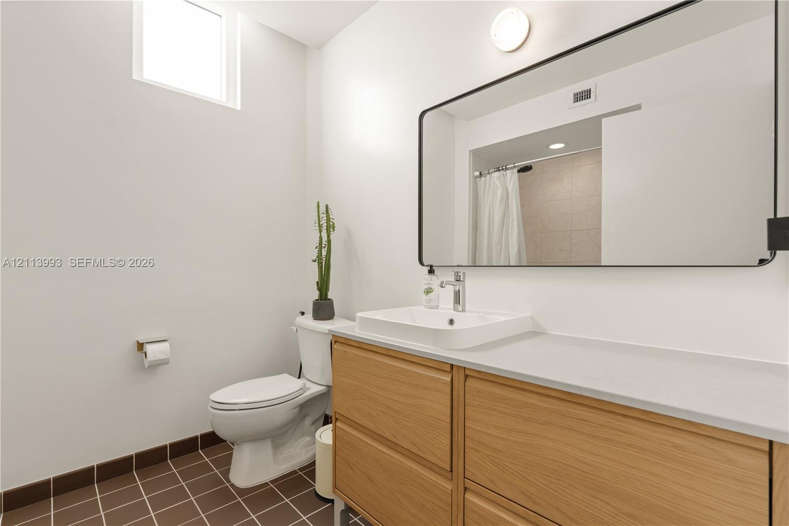 Bathroom featuring a wood-finish vanity with an integrated basin, a large rectangular mirror with a black frame, and tiled flooring