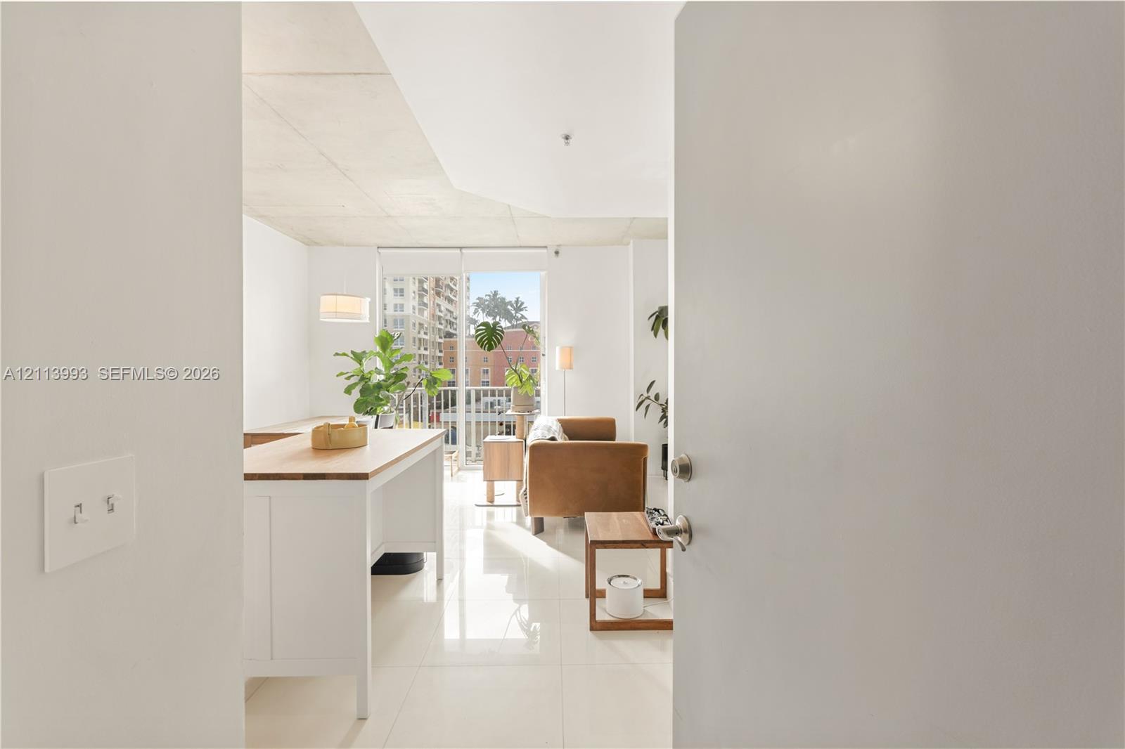 Open-concept living space featuring high ceilings, polished tile flooring, and floor-to-ceiling glass sliding doors opening to a balcony Open-concept living space featuring high ceilings, polished tile flooring, and floor-to-ceiling glass sliding doors opening to a balcony