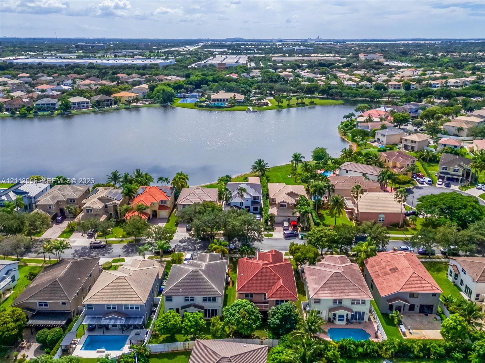 Aerial perspective featuring waterfront residential properties with multi-pitch rooflines, private swimming pools, paved patio areas, and mature landscaping