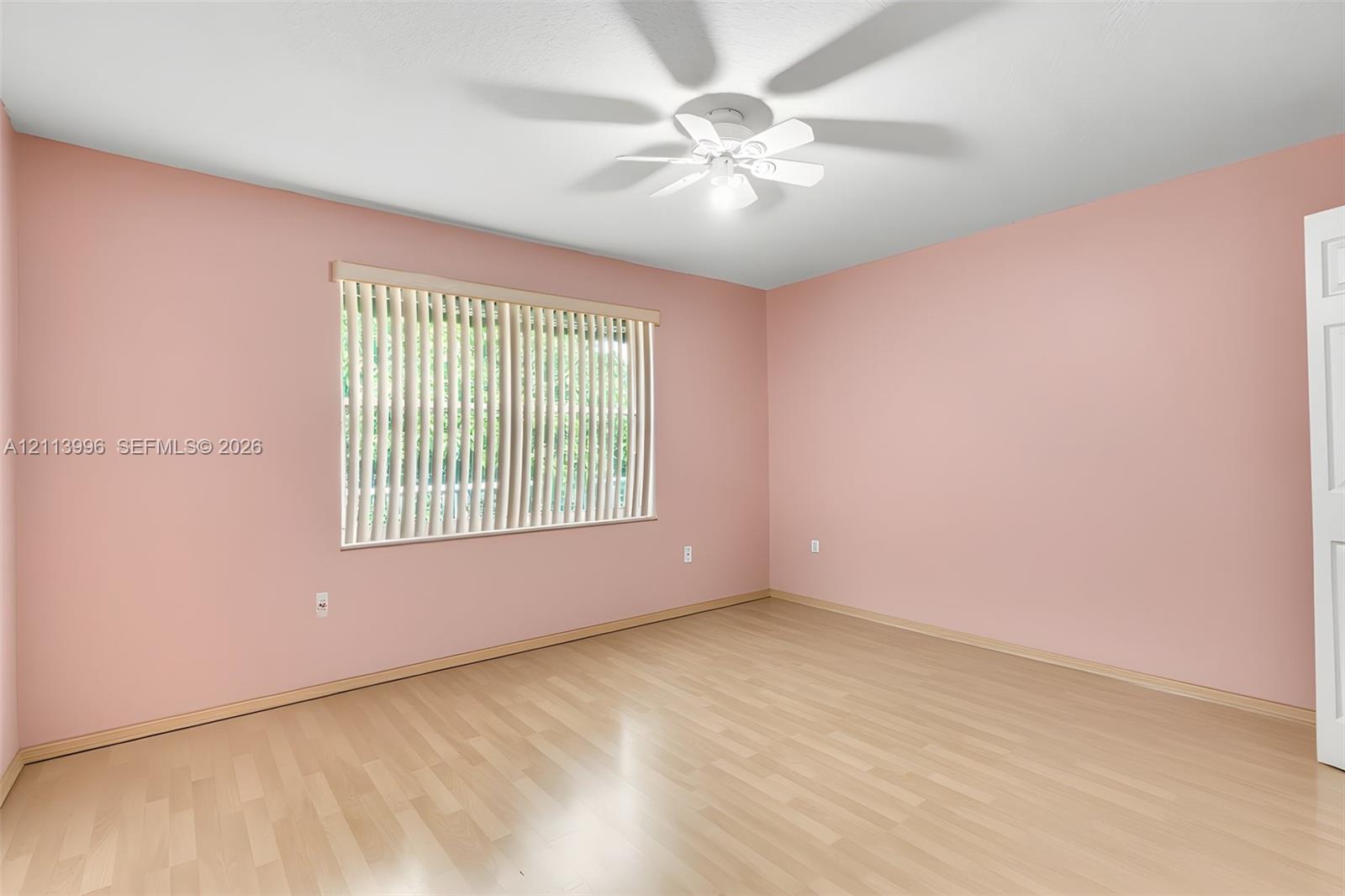 Interior room featuring light wood-finish flooring, a ceiling-mounted fan with integrated lighting, and vertical window blinds
