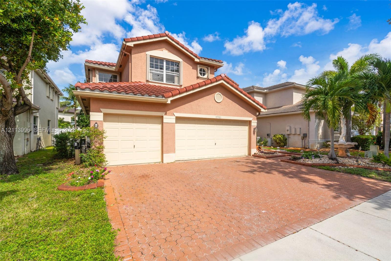 Stucco exterior featuring a terracotta tile roof, multi-car garage, and patterned paver driveway