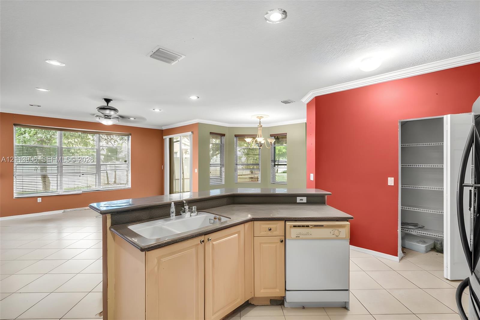 Kitchen island featuring a dual-basin sink, neutral-toned cabinetry, solid surface countertop, built-in dishwasher, and a walk-in pantry