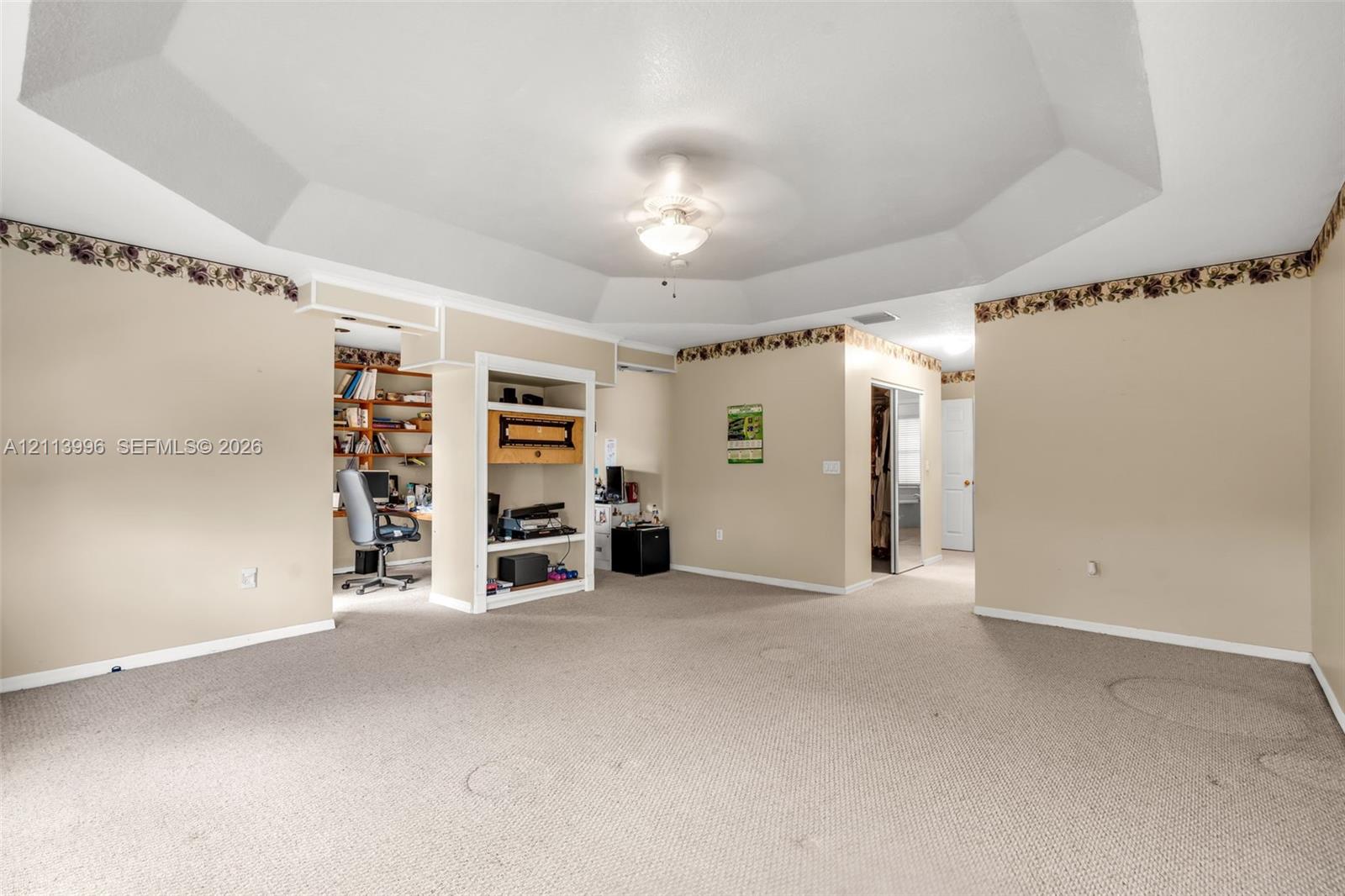 Tray ceiling with central light fixture, wall-to-wall carpeting, and built-in shelving unit