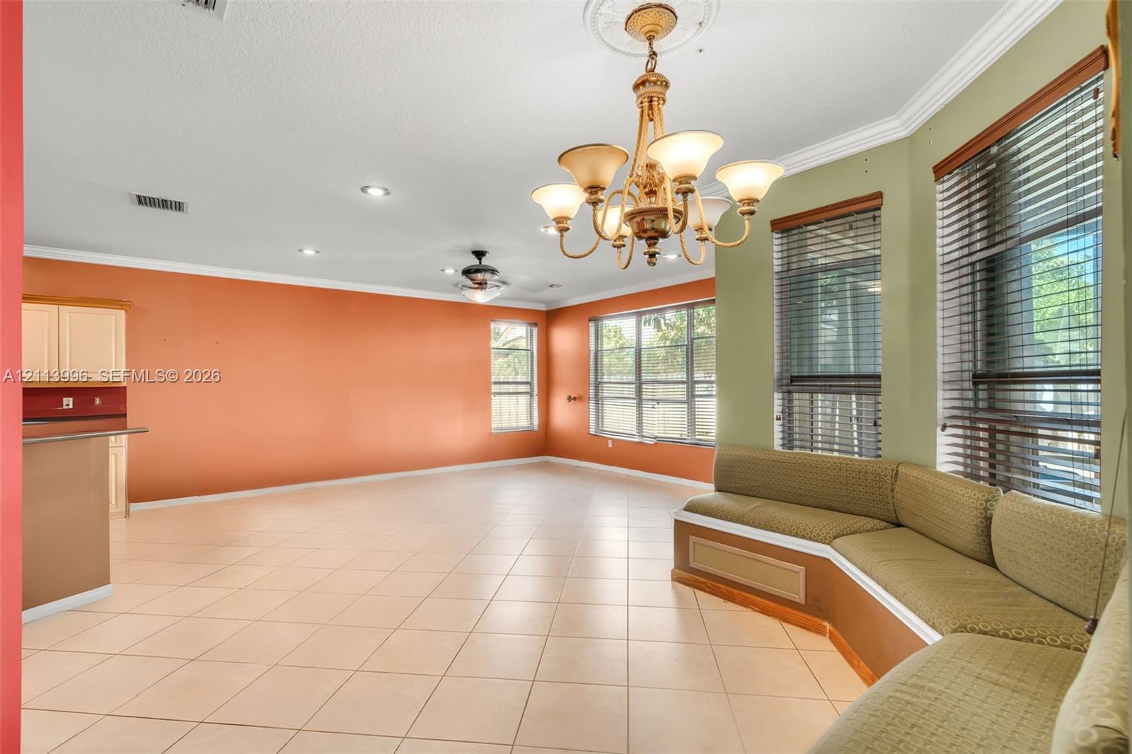 Open-concept room featuring tile flooring, crown molding, a decorative ceiling medallion with an attached multi-arm chandelier, and a custom built-in bench