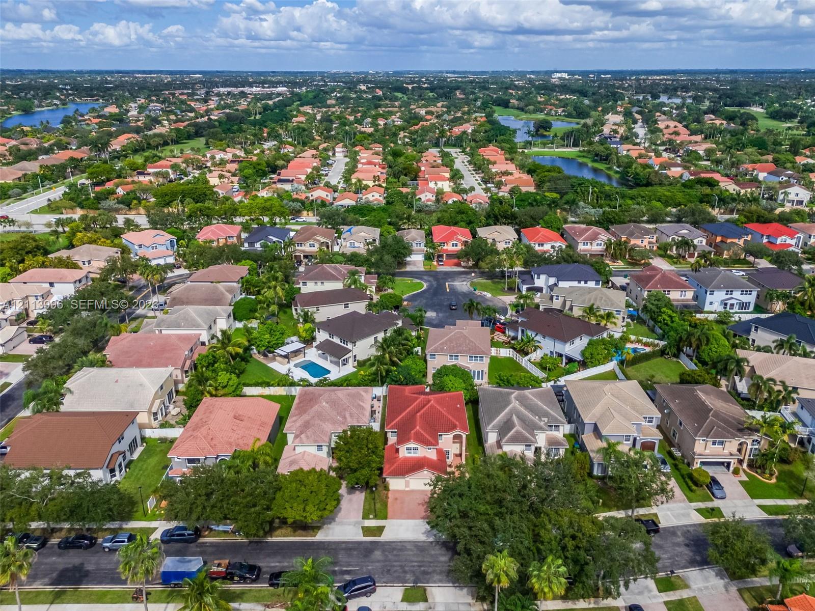 Aerial perspective of a multi-story residence featuring a red tile roof, concrete driveway, and attached garage within a landscaped residential neighborhood