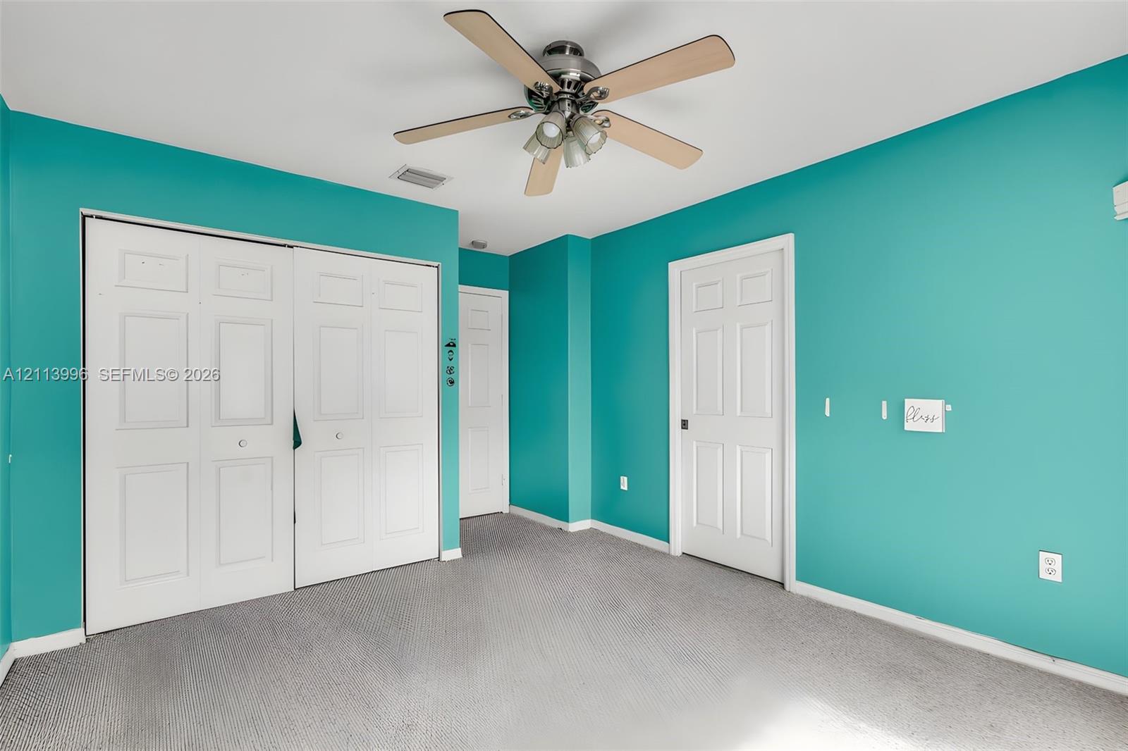 Room featuring gray carpeting, a multi-blade ceiling fan with integrated light fixture, and double-panel closet doors