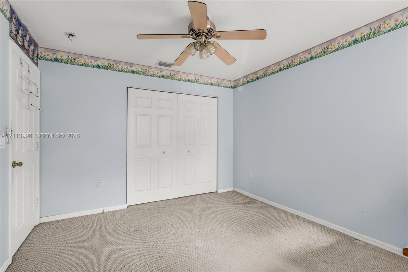 Room featuring neutral carpeting, a ceiling-mounted fan with integrated lighting, and a double-panel closet with white doors