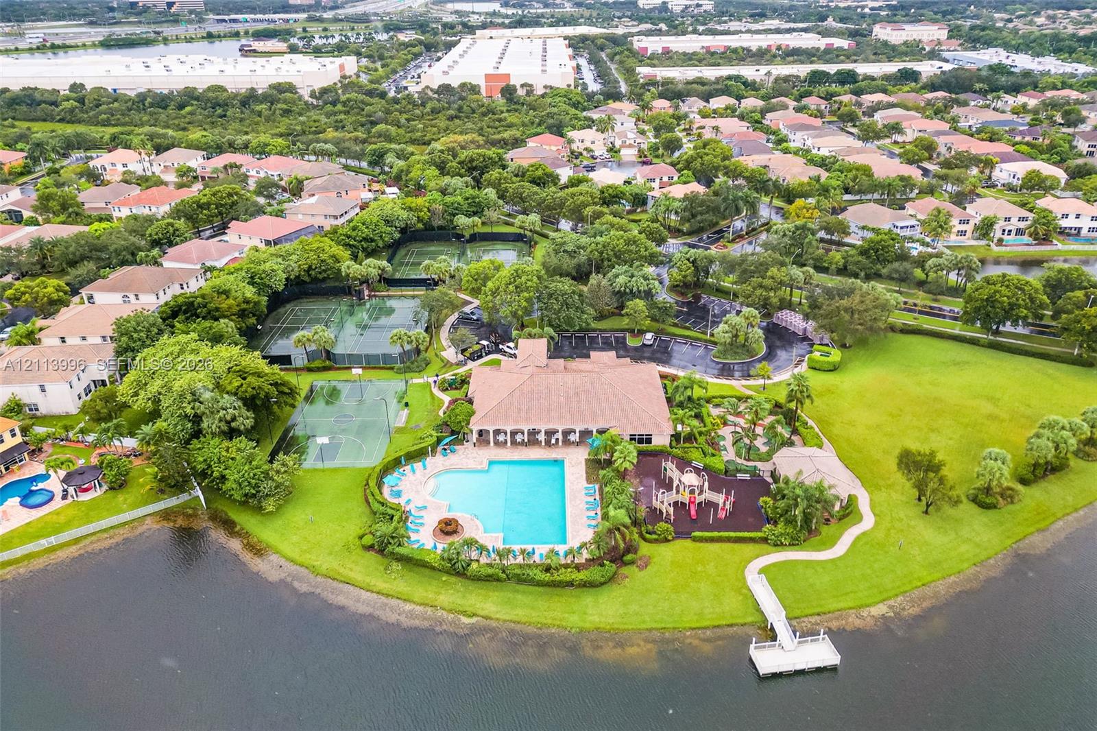 Aerial perspective of community clubhouse amenities featuring an outdoor swimming pool, tennis courts, playground equipment, and a private dock extending into the water