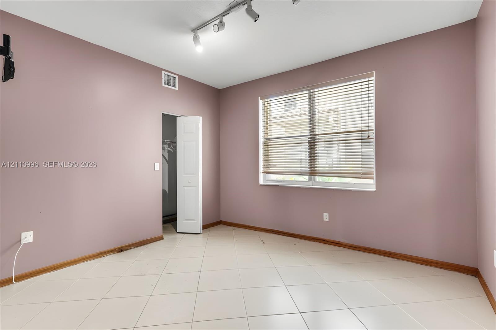Room featuring neutral-toned walls, light-colored tile flooring, track lighting, and a closet with bifold doors
