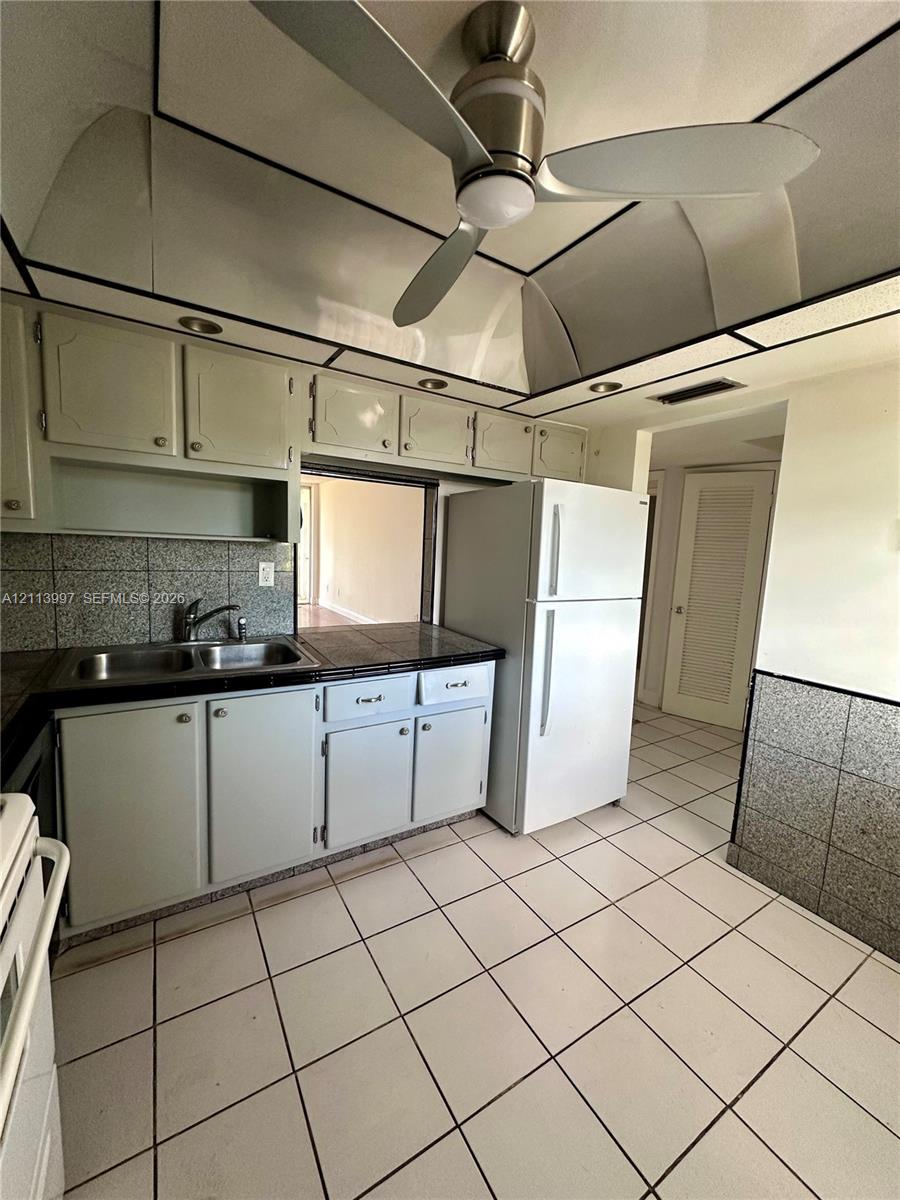 Kitchen featuring custom cabinetry, tile backsplash, built-in ceiling fan, and tiled flooring