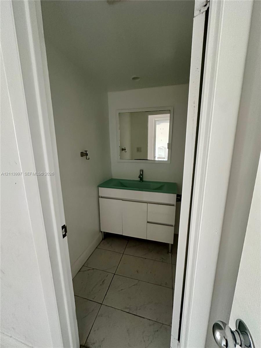 White vanity with integrated colored sink, rectangular wall-mounted mirror, and large-format tile flooring