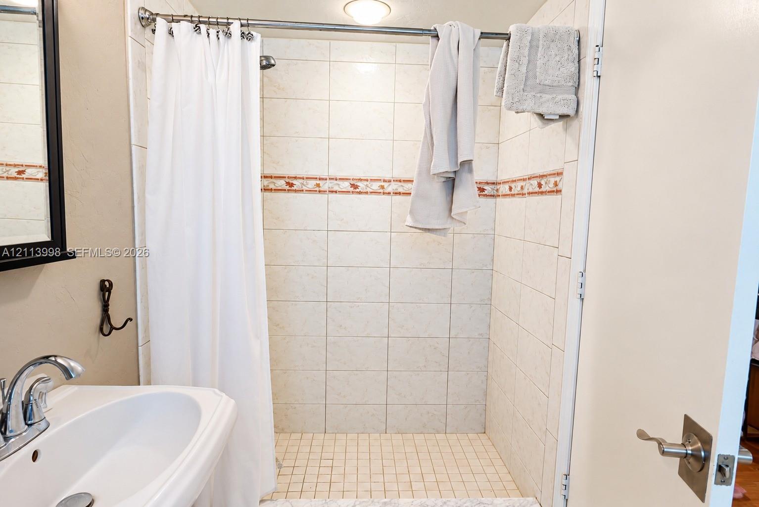 Bathroom featuring a wall-mounted sink with a chrome finish faucet, a tile-surround shower with an integrated decorative accent border, and a square tile shower floor