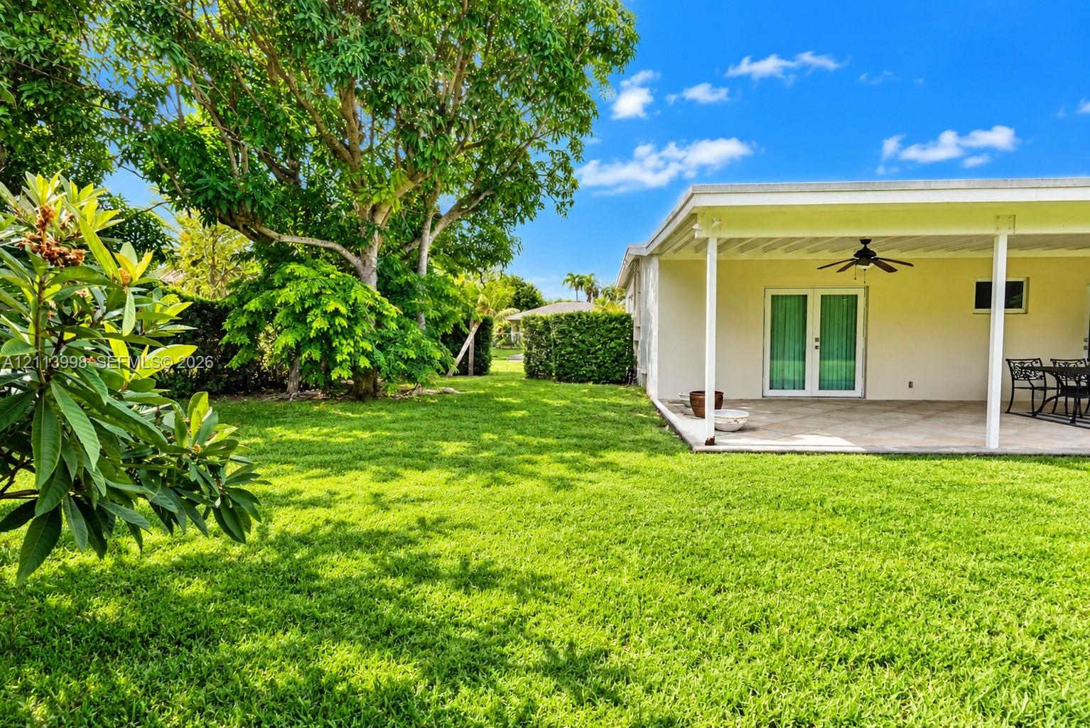 Expansive backyard featuring a manicured lawn, mature trees, and a covered patio with a ceiling fan