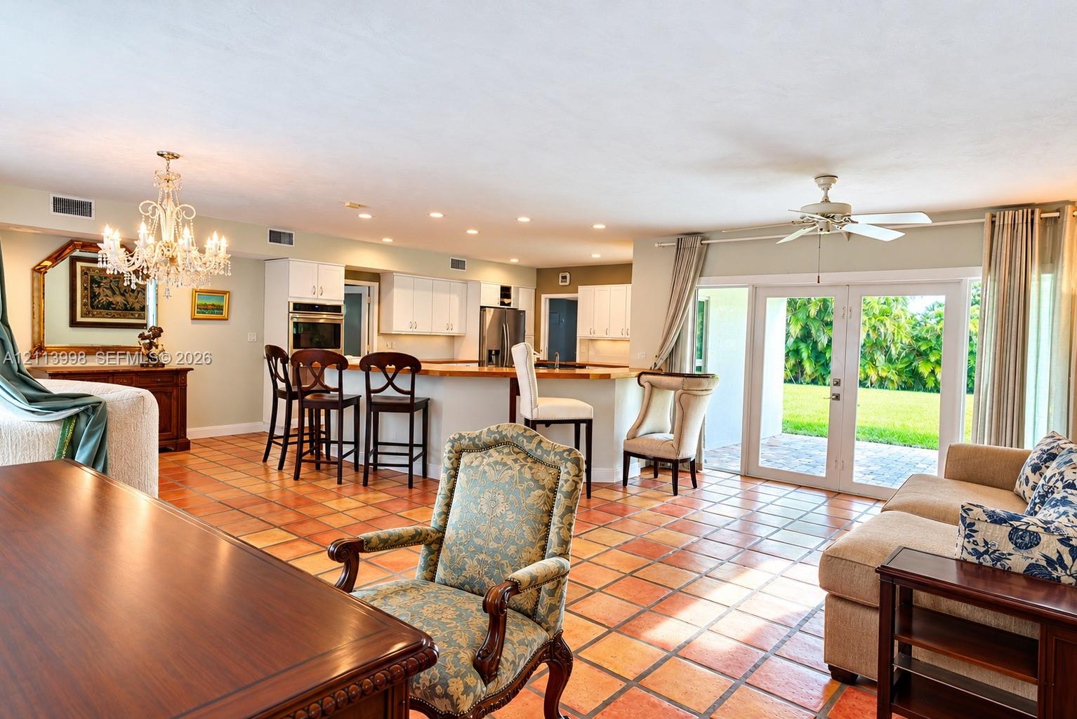 Open-concept kitchen and living area featuring ceramic tile flooring, built-in wall oven, multi-level breakfast bar, and glass-paneled double doors providing outdoor access