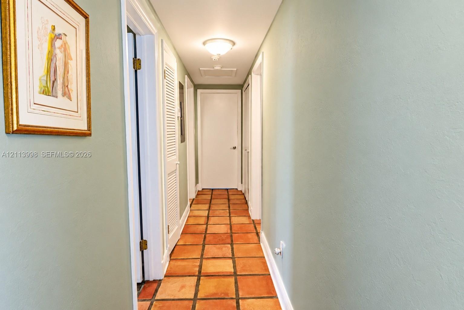 Hallway featuring terracotta tile flooring, smooth-finish walls, and white louvered closet doors