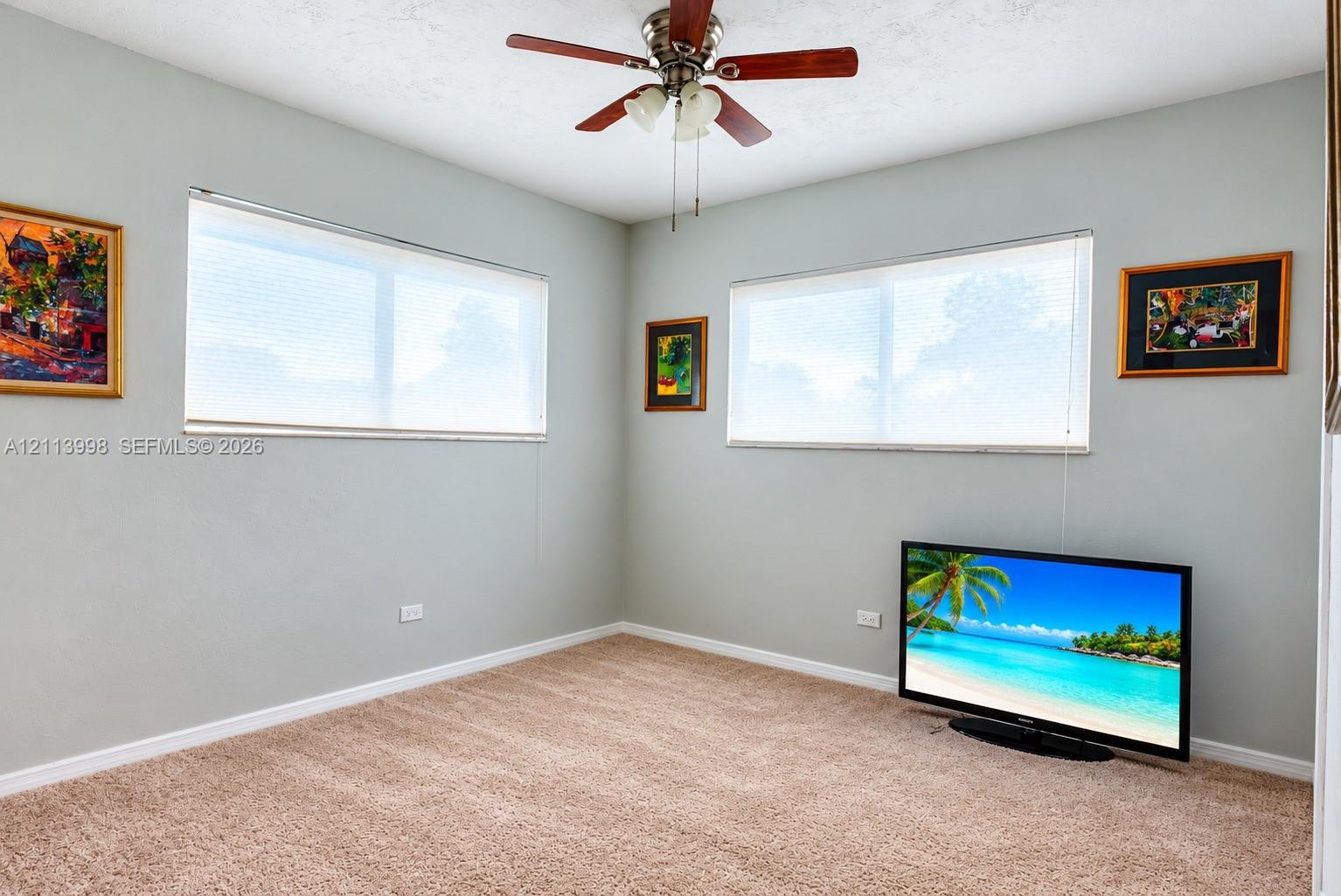 Neutral-toned walls, wall-to-wall carpeting, dual windows with fitted blinds, and a multi-blade ceiling fan with an integrated light fixture