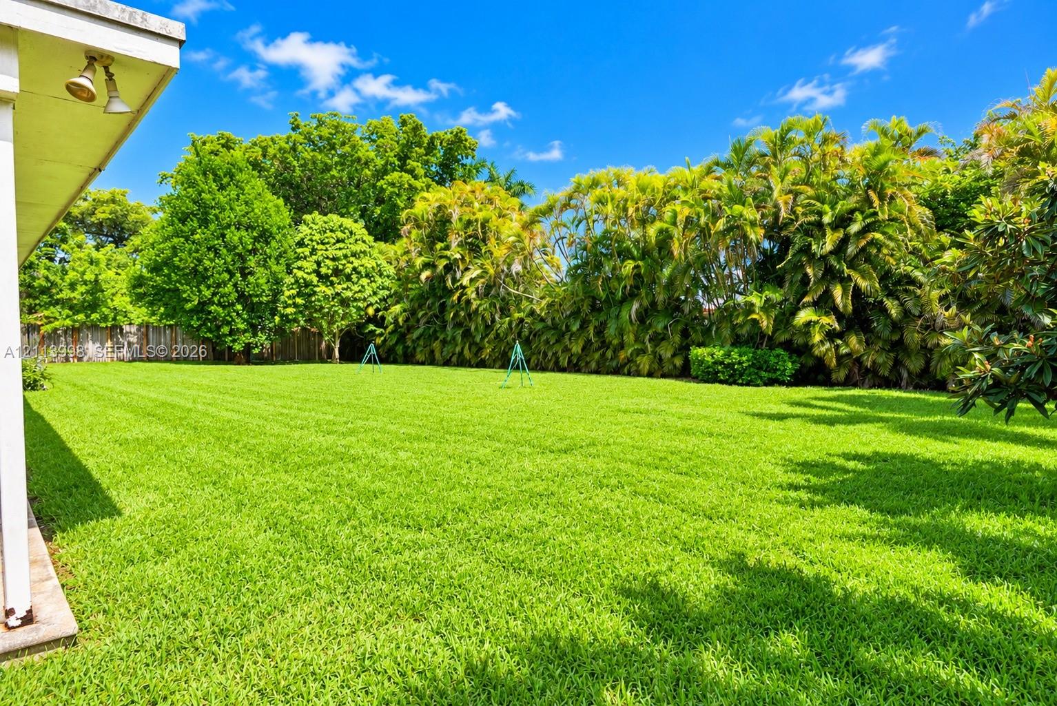 Expansive backyard featuring a manicured lawn, perimeter fencing, and mature landscaping