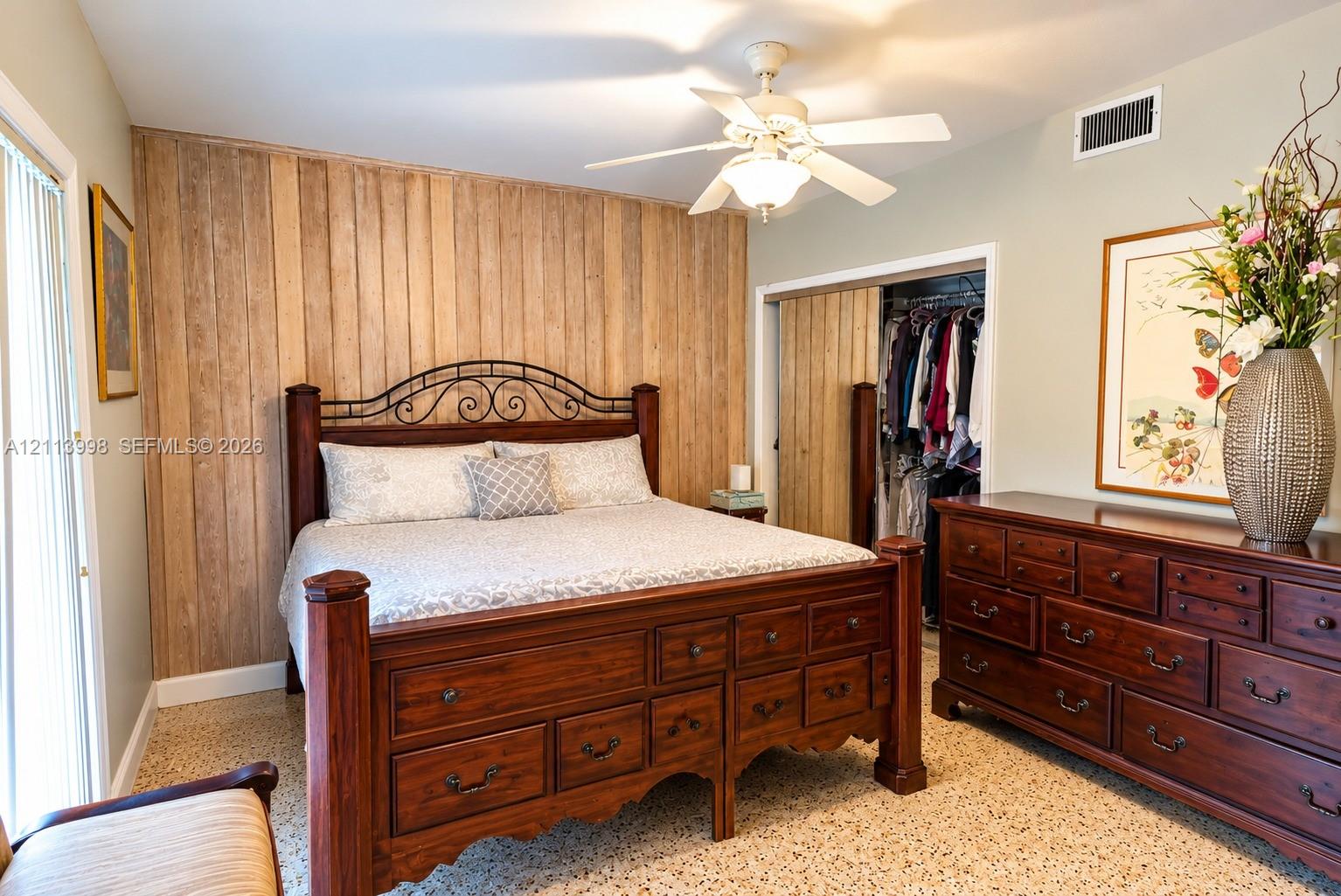 Vertical wood-plank accent wall, sliding closet doors with matching wood finish, neutral wall paint, overhead ceiling fan with light fixture, and terrazzo flooring