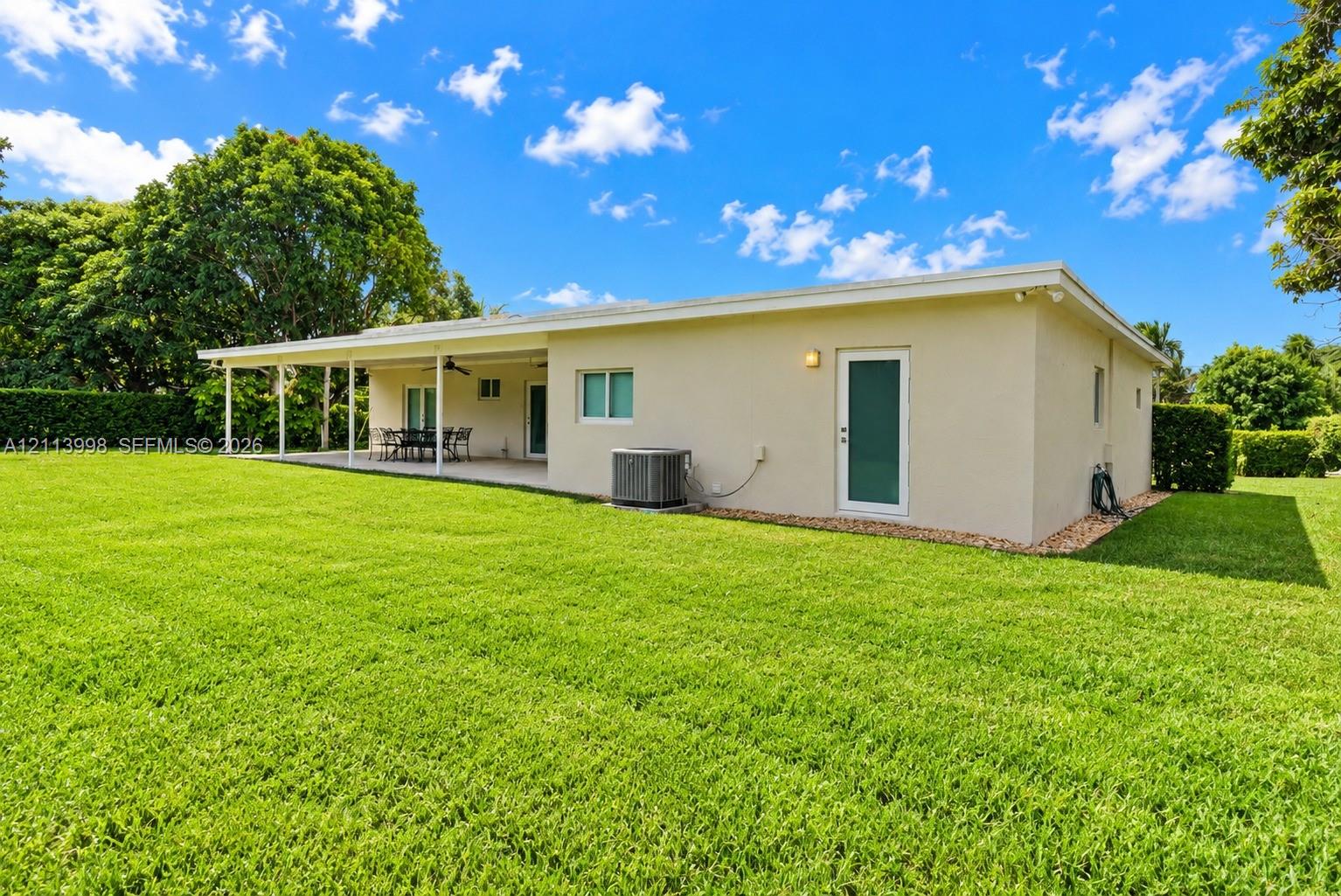 Spacious backyard featuring a manicured lawn, expansive covered patio, and mature perimeter landscaping