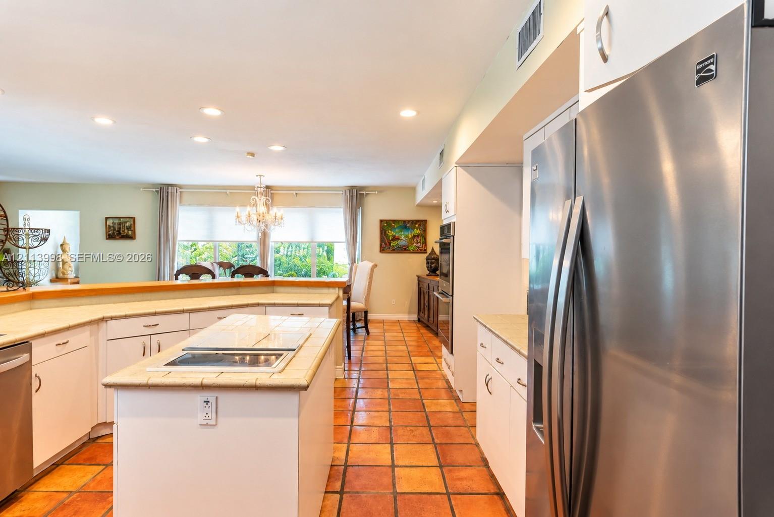 Kitchen featuring a central island with a tiled countertop, stainless steel refrigerator, white cabinetry, integrated wall oven, and ceramic tile flooring