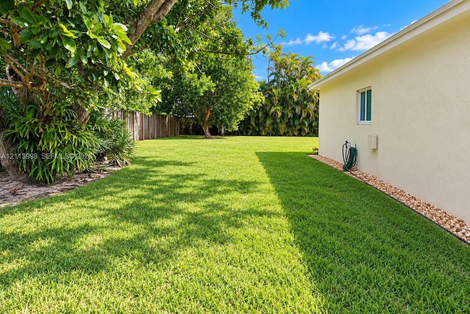 Expansive grassy side yard featuring mature landscaping, wood-tone fencing, and decorative stone ground cover