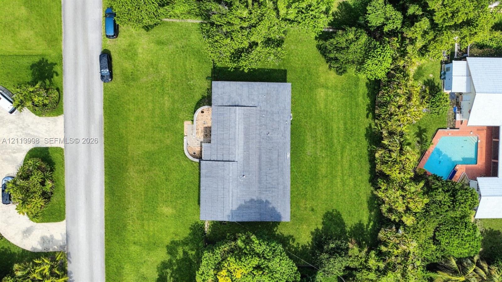 Aerial perspective featuring a spacious lot with mature perimeter trees, expansive lawn, and a paved walkway