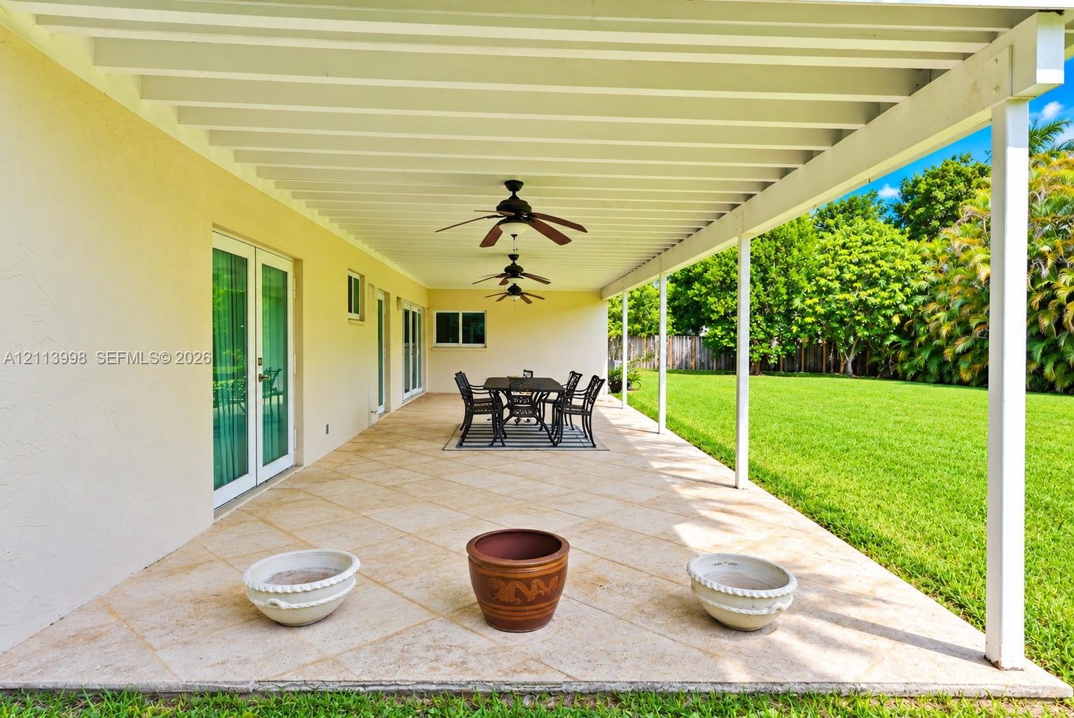 Covered outdoor patio featuring tile flooring, ceiling fans, structural support posts, and double glass doors