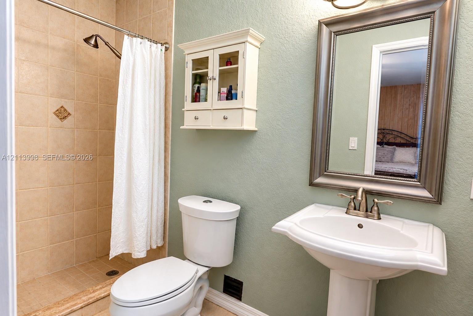 Pedestal sink with metallic faucet, wall-mounted cabinet, and tile-surround shower