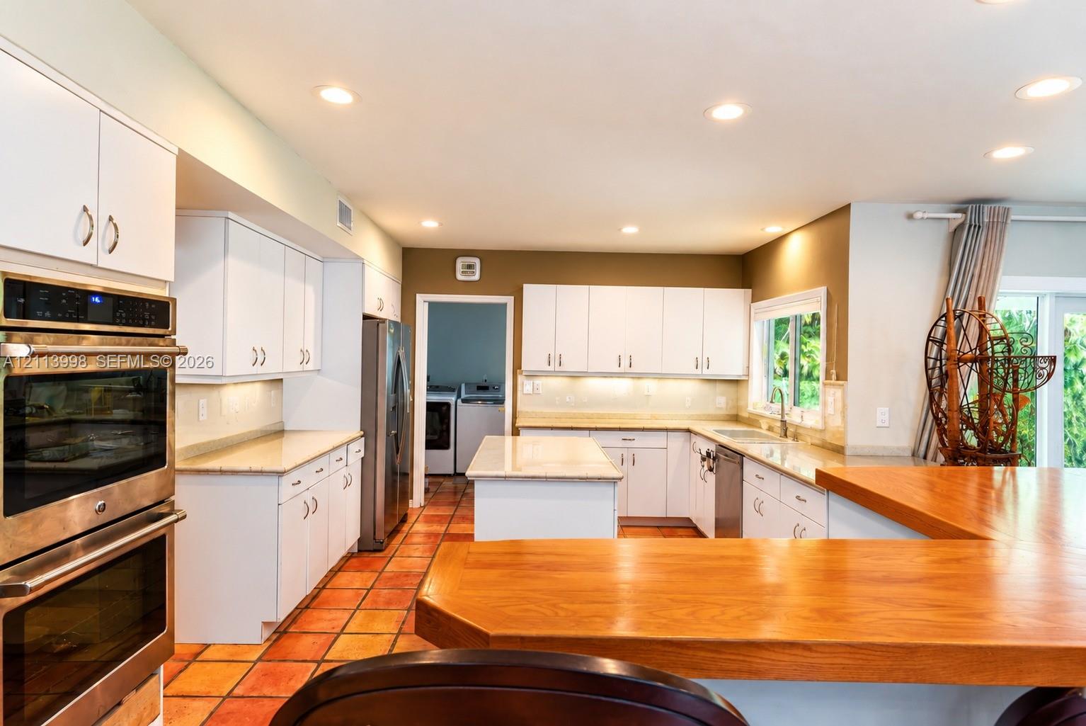 Kitchen featuring white cabinetry, stone-finish countertops, stainless steel double wall ovens, a center island, and ceramic tile flooring