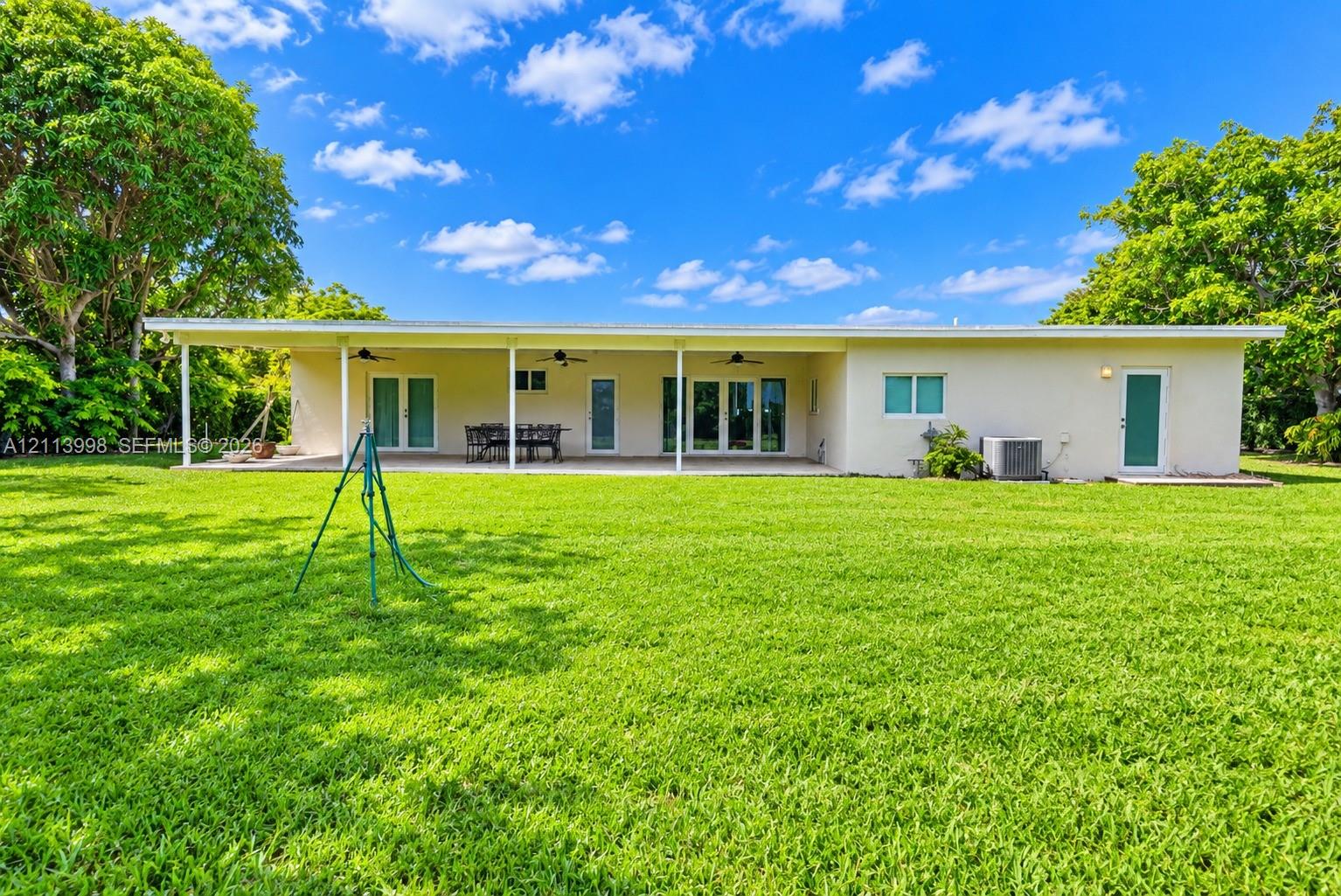 Rear exterior featuring a covered patio, multiple glass-panel doors, ceiling fans, and an expansive lawn