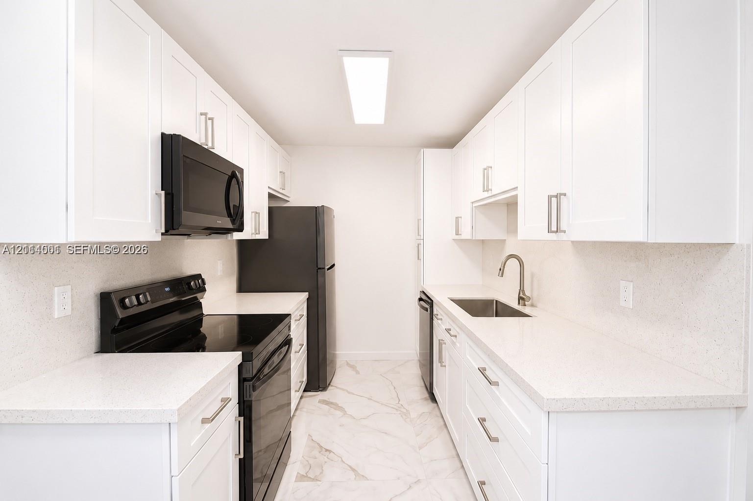 Galley kitchen featuring white Shaker-style cabinetry, solid-surface countertops, black appliances, a stainless steel undermount sink, and stone-finish tile flooring