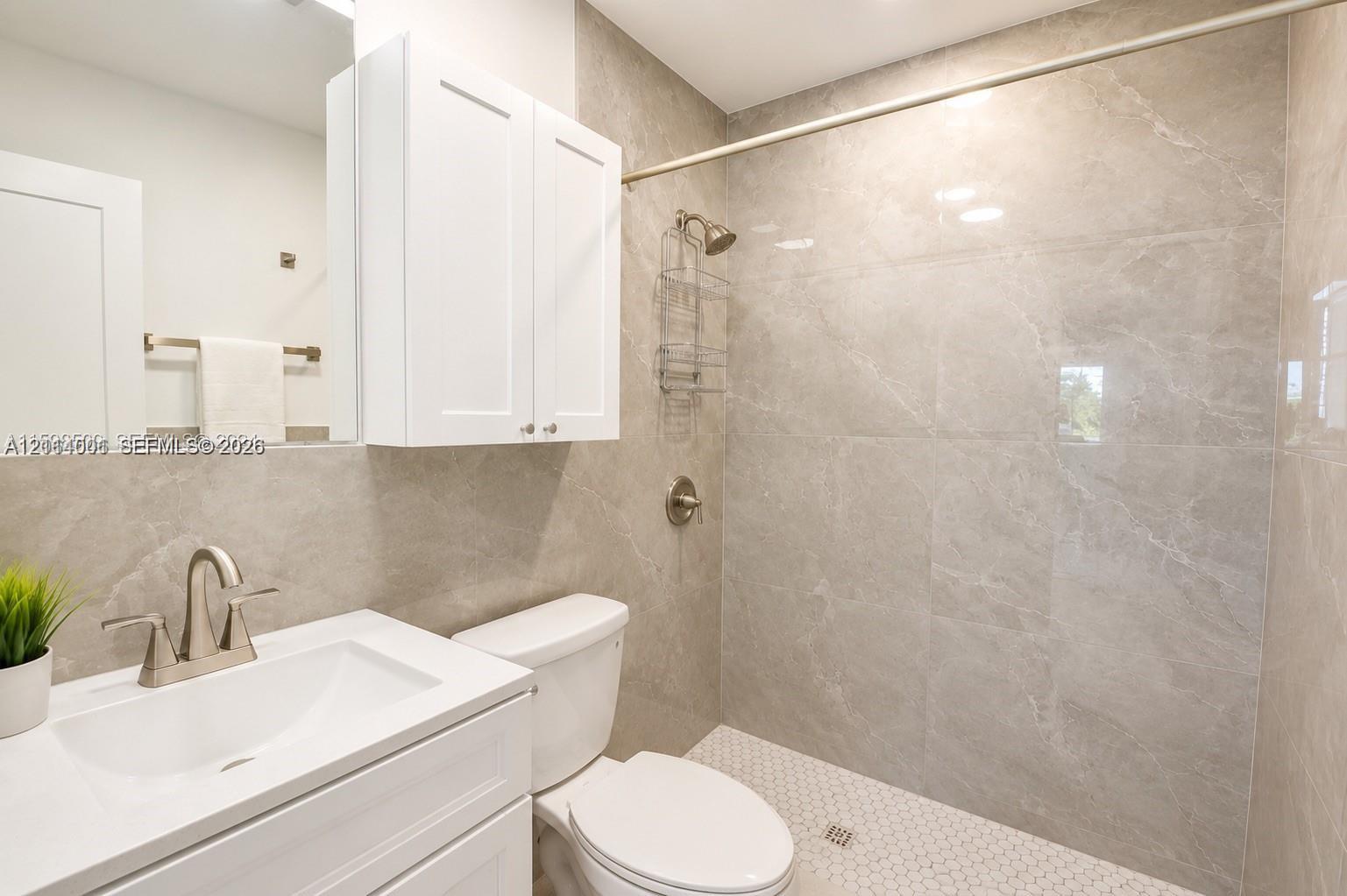 Bathroom featuring large-format gray tiled shower walls, white vanity cabinet with a integrated sink, polished chrome faucet, and geometric tile shower flooring