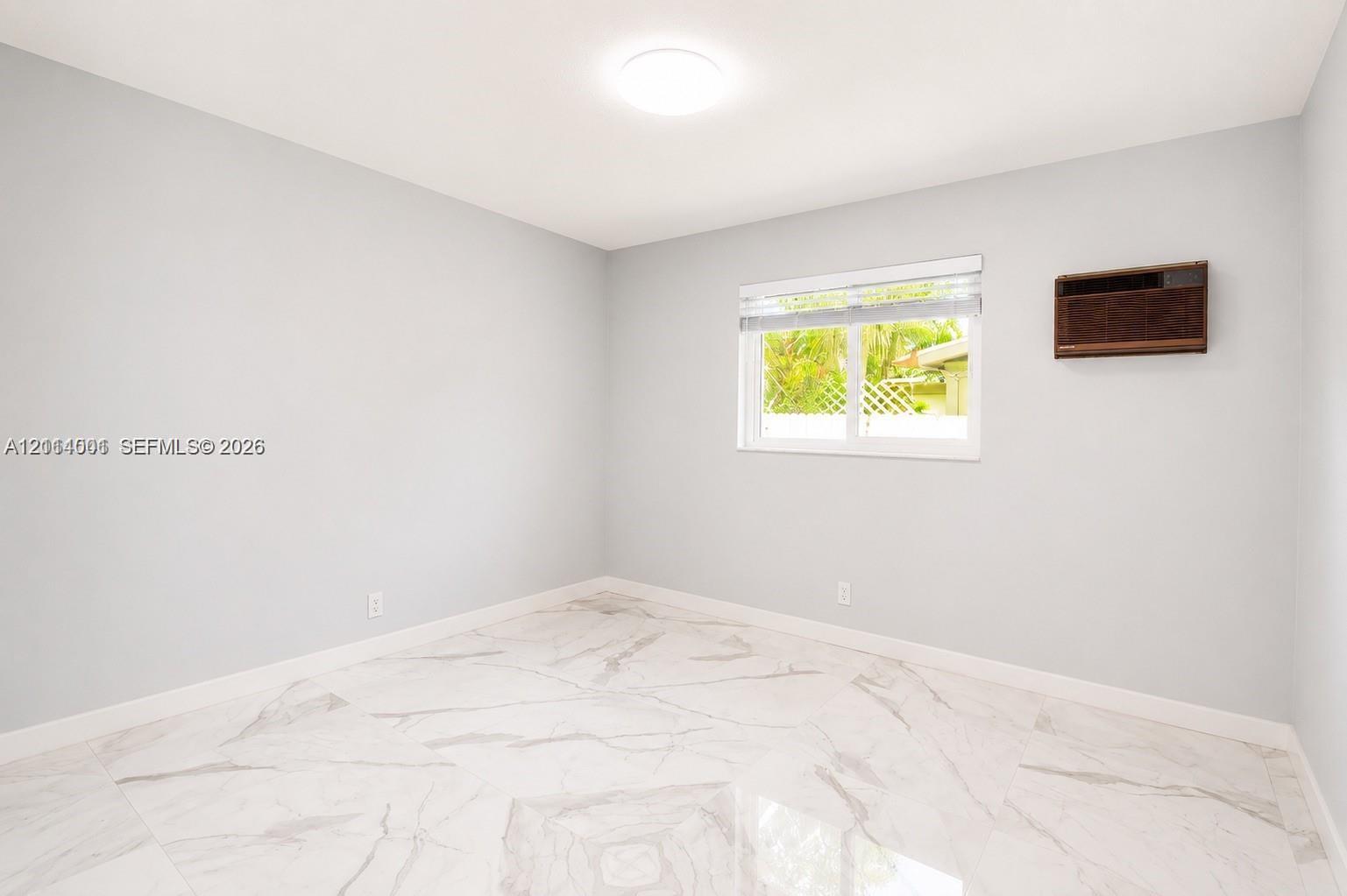Room featuring large-format light-toned stone-finish flooring, neutral wall paint, a ceiling-mounted light fixture, and a window with horizontal blinds