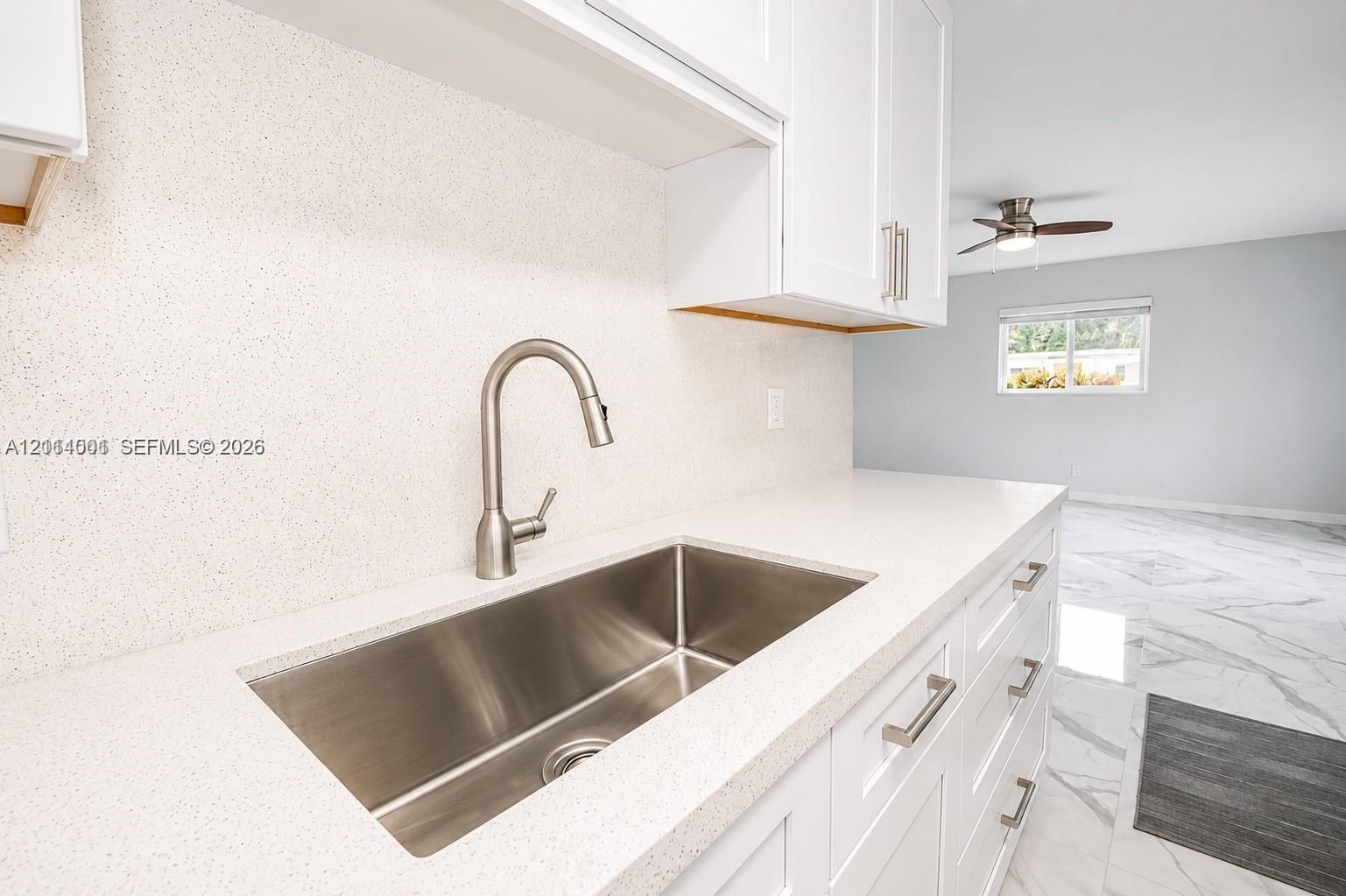 Stainless steel undermount sink with a gooseneck pull-down faucet, quartz countertops, white shaker-style cabinetry, and polished stone-finish flooring
