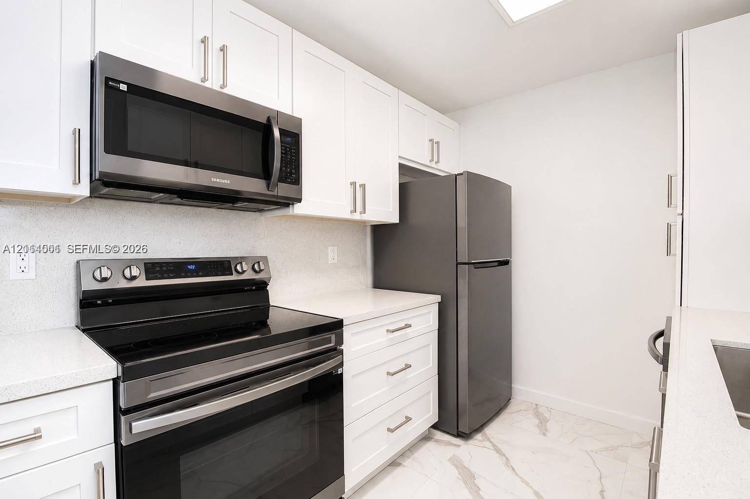 Kitchen featuring white shaker-style cabinetry, solid-surface countertops, stainless steel appliances, and large-format tile flooring with veining