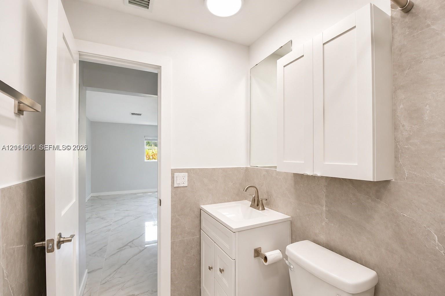 Bathroom featuring a white vanity cabinet with an integrated sink, brushed nickel faucet, wall-mounted medicine cabinet, and full-height stone-finish wall tile