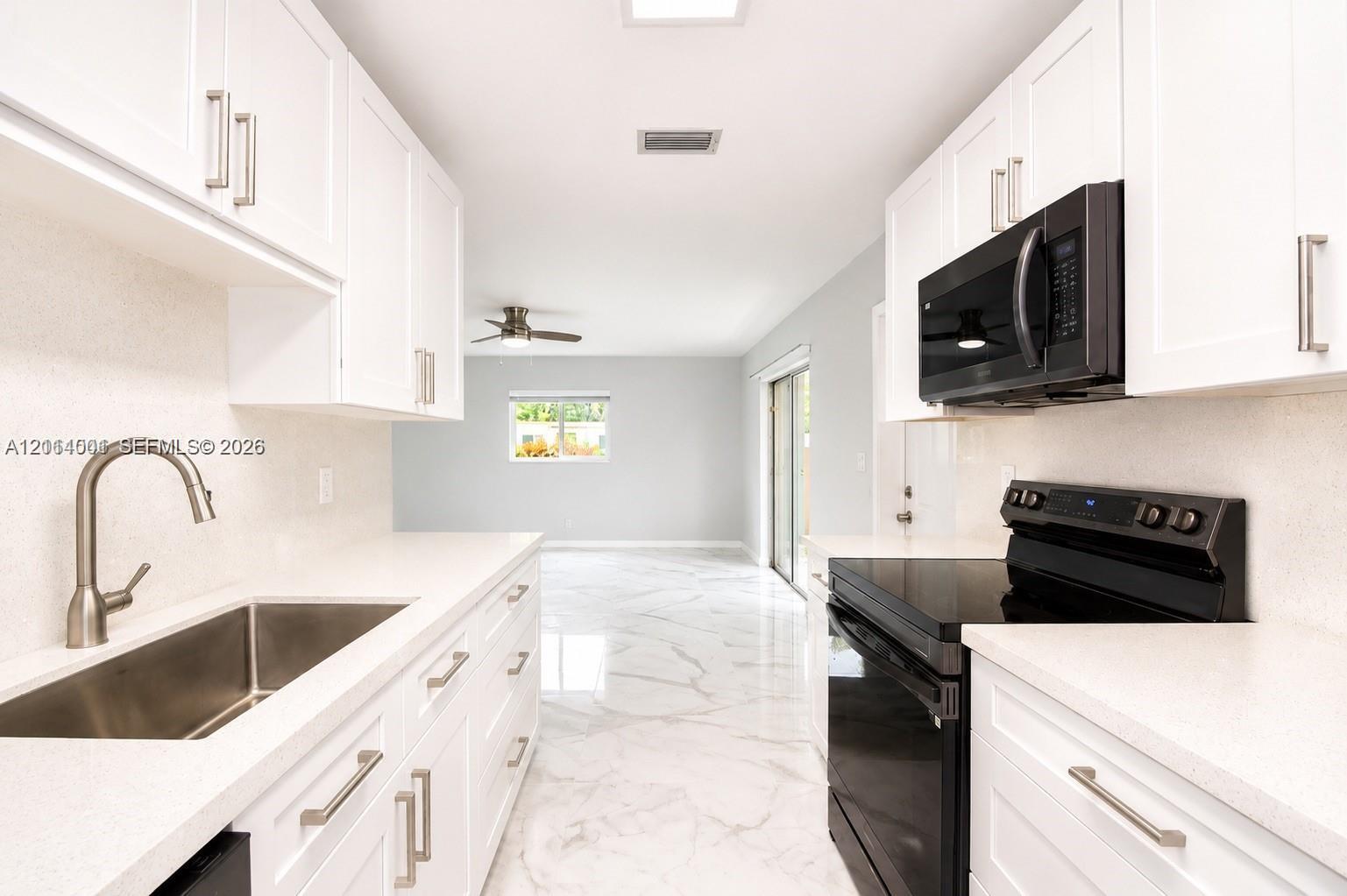 Kitchen featuring white Shaker-style cabinetry, solid-surface countertops, an undermount stainless steel sink with a high-arch faucet, black appliance suite, and polished stone-finish flooring Kitchen featuring white Shaker-style cabinetry, solid-surface countertops, an undermount stainless steel sink with a high-arch faucet, black appliance suite, and polished stone-finish flooring