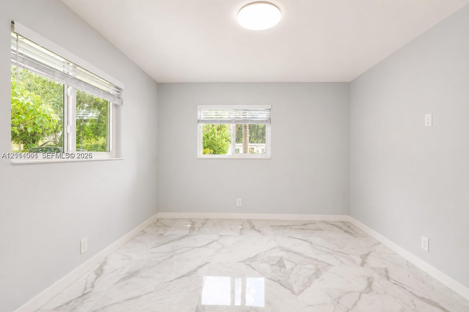 Neutral-toned interior room featuring large-format stone-finish tile flooring, two horizontal sliding windows, and a central flush-mount ceiling light fixture