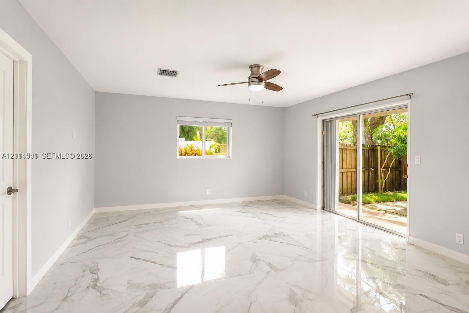 Interior space featuring light-toned flooring with natural veining patterns, sliding glass doors, and a ceiling fan with integrated lighting