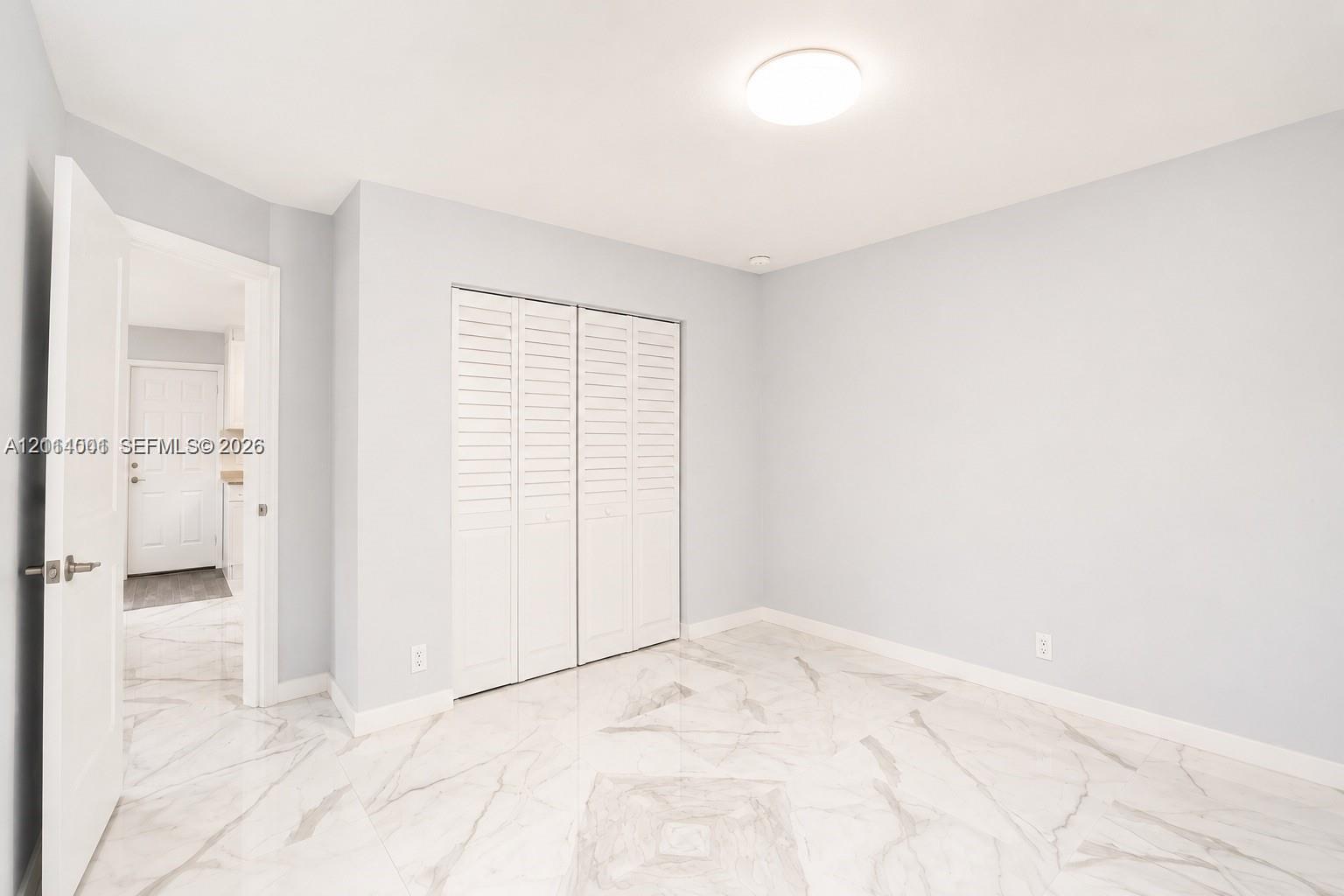 Interior space featuring polished stone-finish flooring, white louvered-style closet doors, and a flush-mount ceiling light fixture