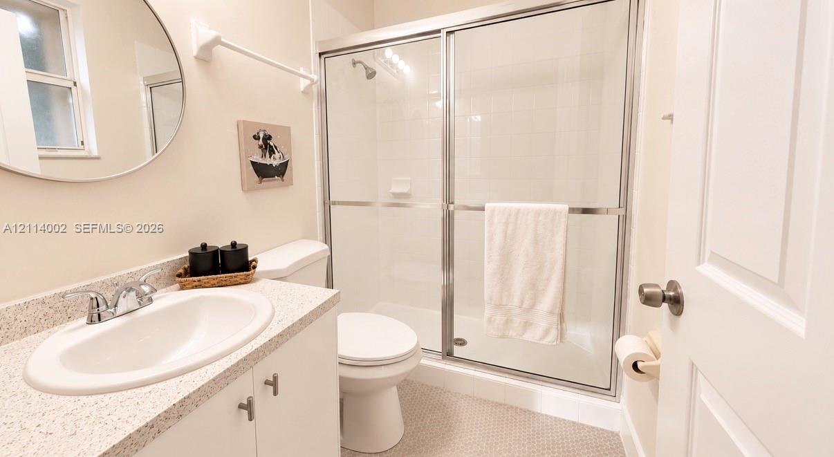 Bathroom featuring a vanity with a stone-composite countertop, oval undermount sink, chrome faucet, circular mirror, and a shower enclosure with sliding glass doors