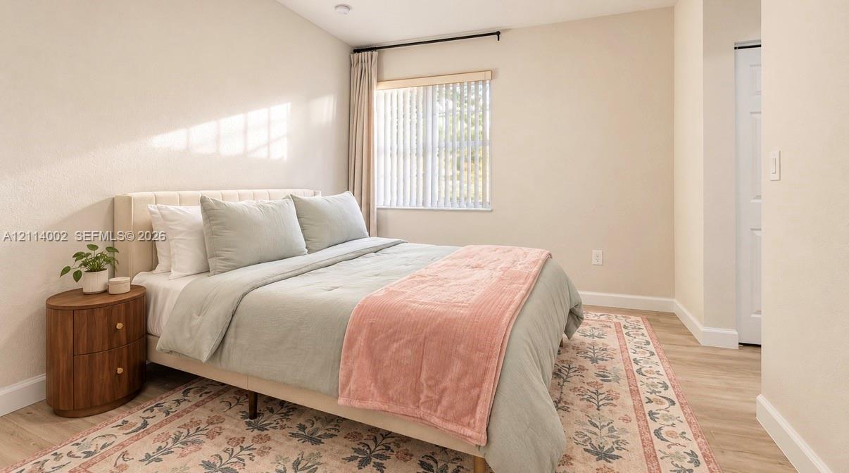 Neutral-toned room featuring light wood-finish flooring, a vaulted ceiling, and a window with vertical blinds