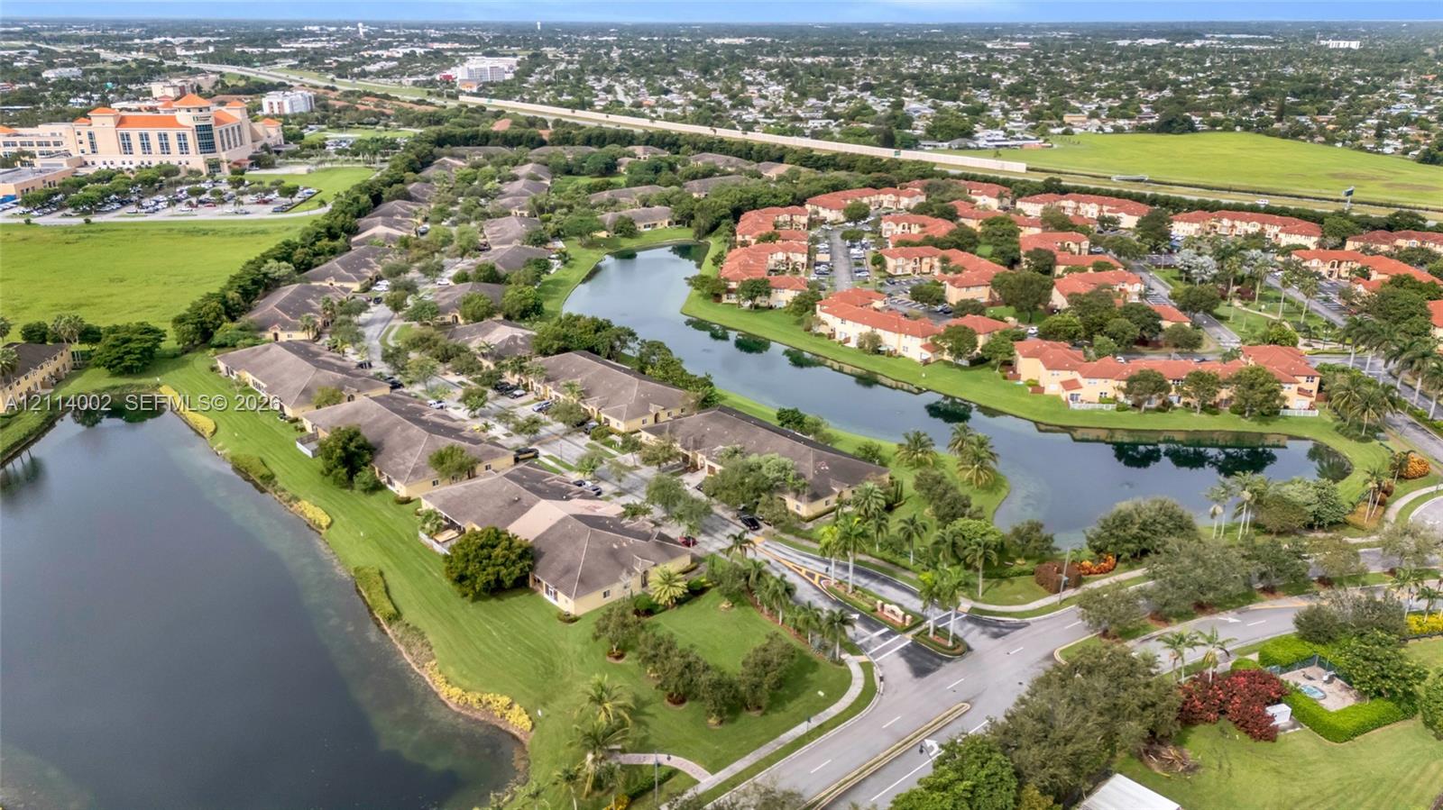 Aerial perspective of a multi-unit residential community featuring terracotta-style roofs, expansive water frontage, paved access roads, and mature perimeter landscaping