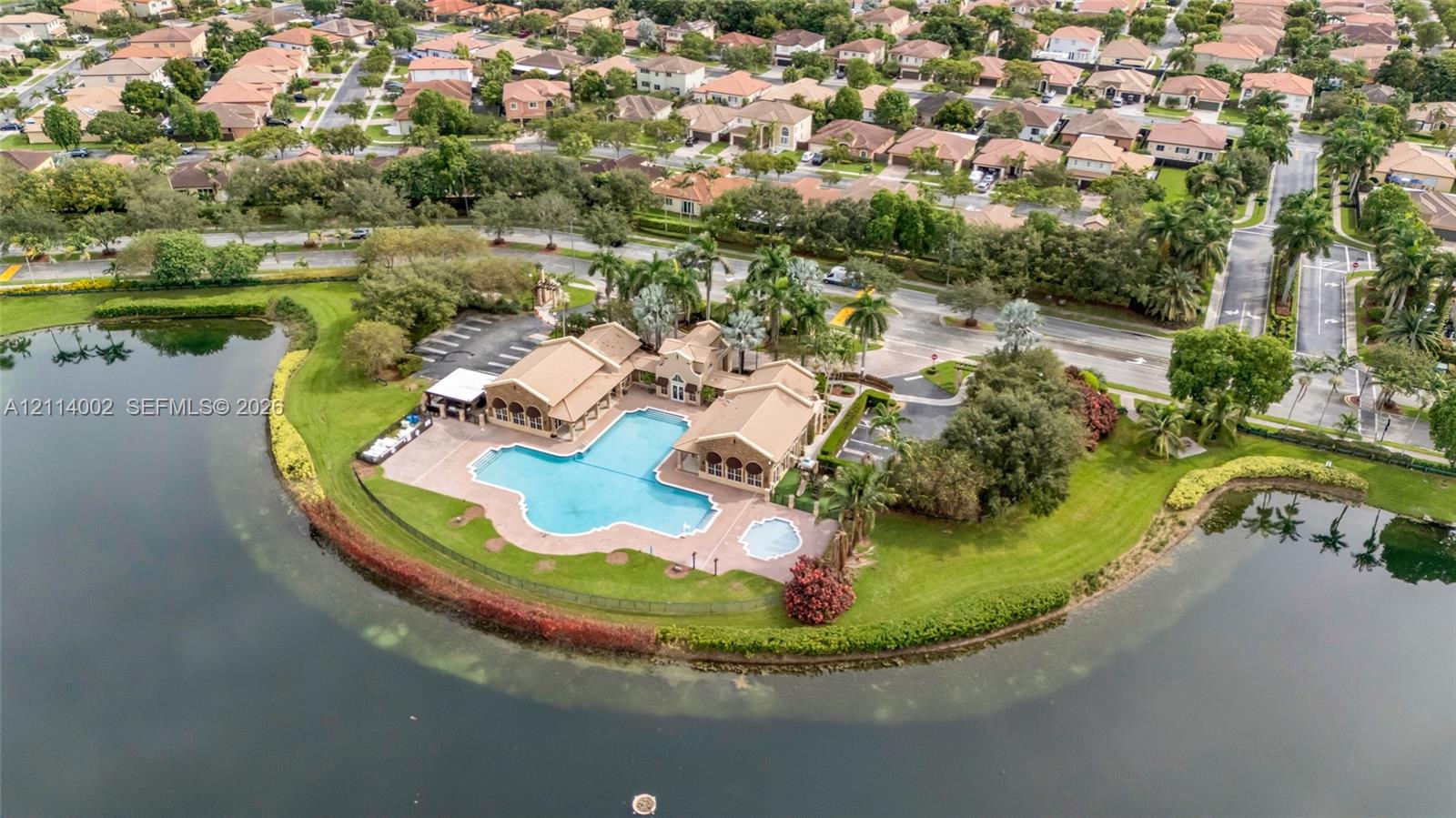 Waterfront clubhouse facility featuring an expansive swimming pool, integrated spa, paved pool deck, and perimeter landscaping