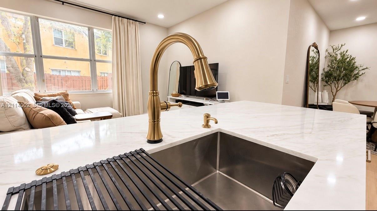 Kitchen island featuring a stone-look countertop, undermount stainless steel sink, and high-arc faucet in a brass finish