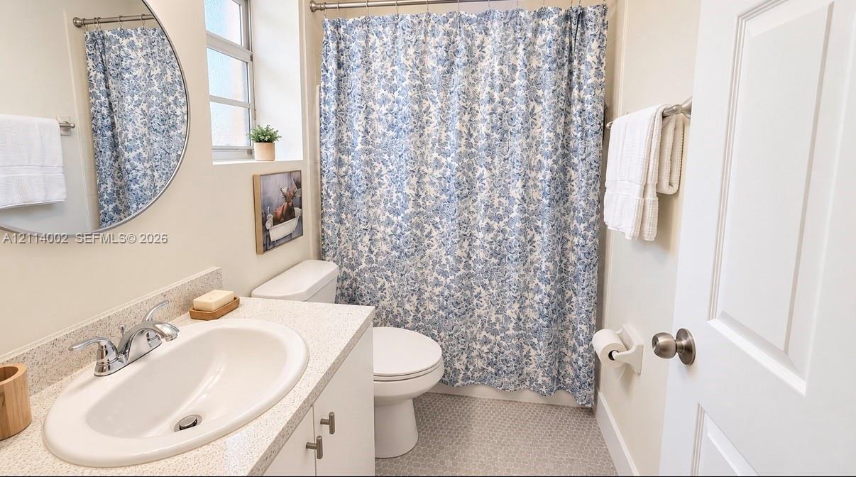 Bathroom featuring a vanity with a neutral solid-surface countertop, an integrated oval basin, a round wall-mounted mirror, and tile flooring