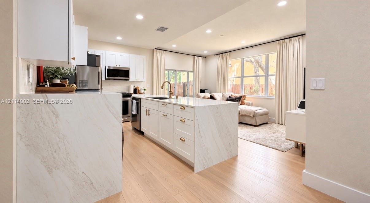 Kitchen featuring a waterfall-edge stone countertop, shaker-style cabinetry, stainless steel appliances, and wood-finish flooring